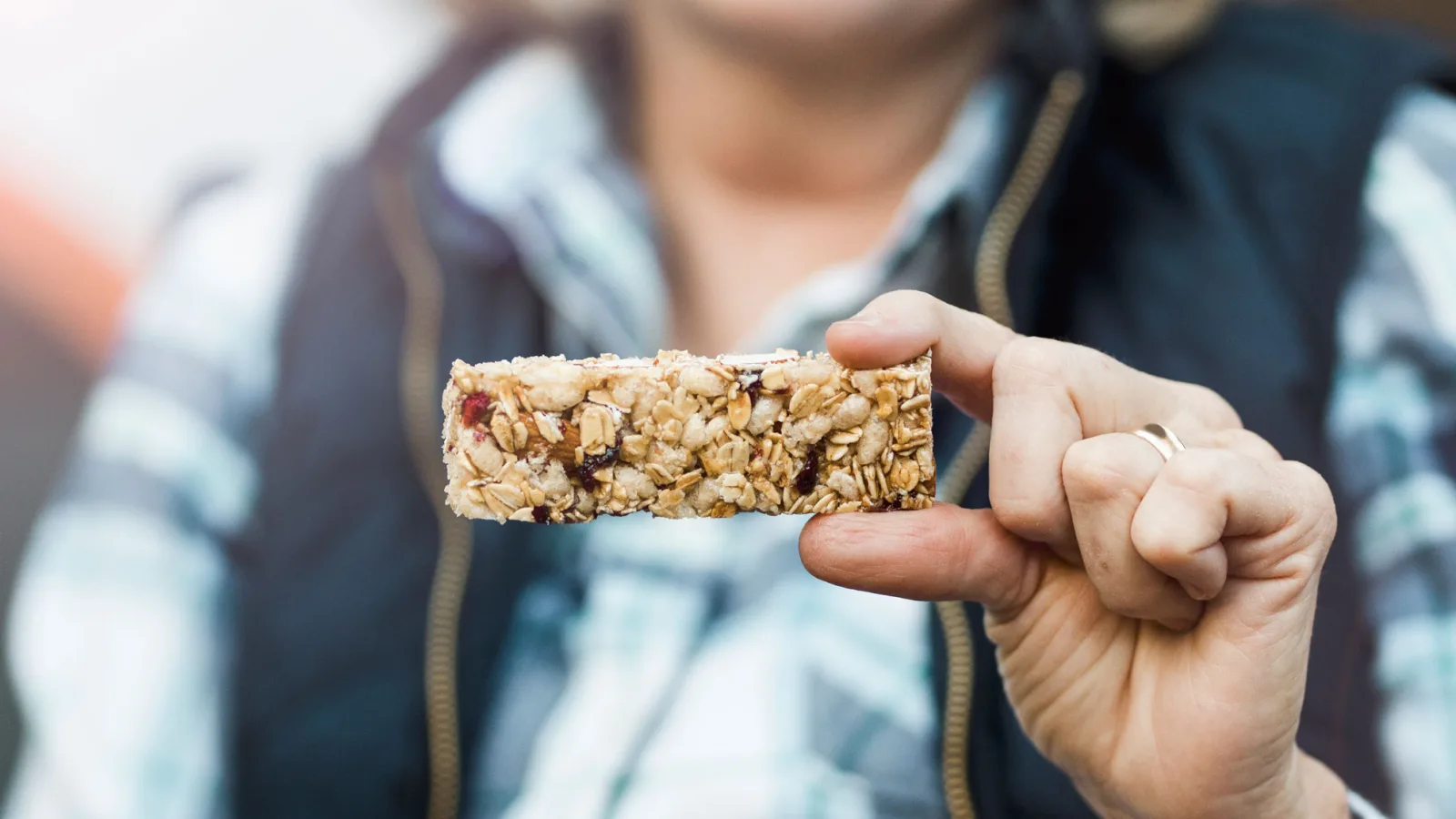 Close-up of a hand holding an oat and berry granola bar at camp