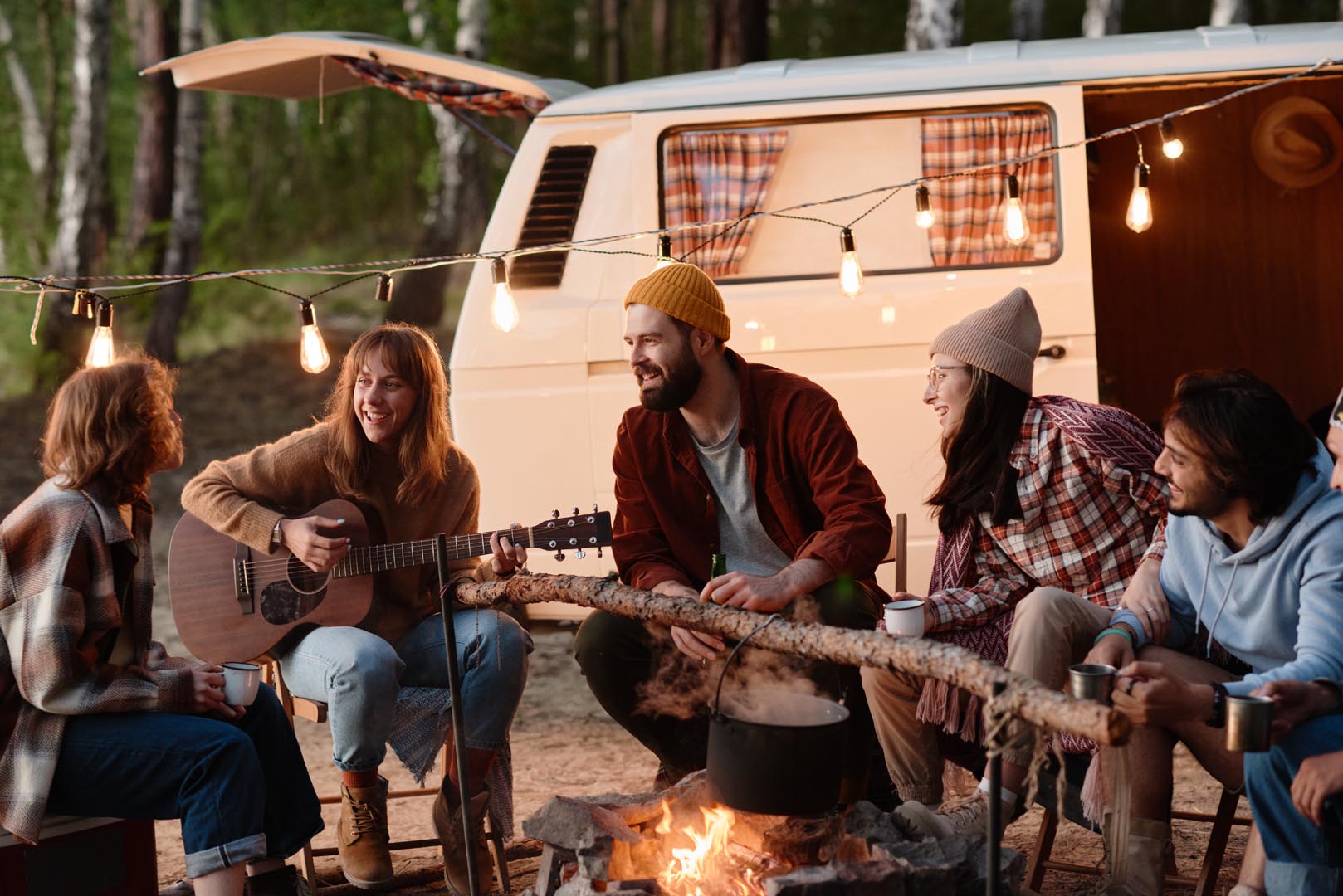 Group friends sitting near fire playing guitar together picnic nature