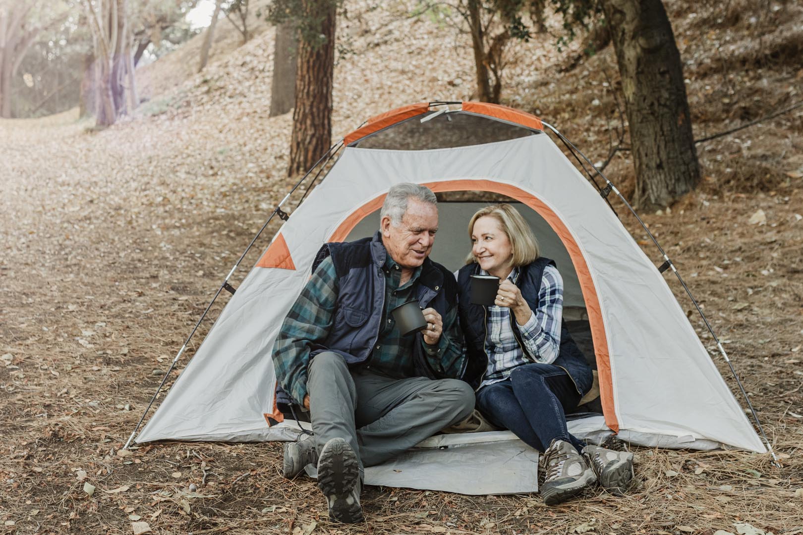 Happy old couple having coffee by tent forest