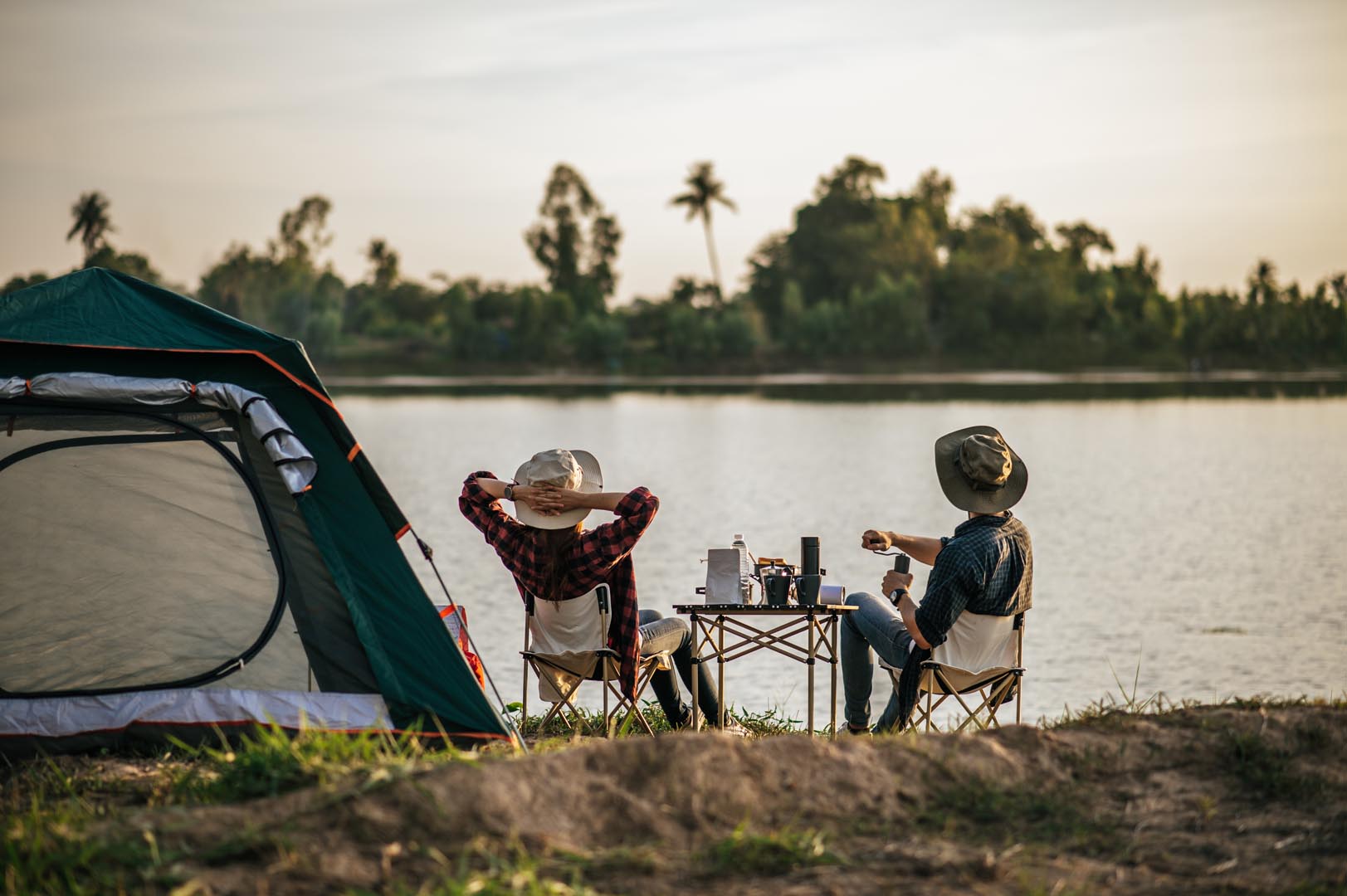 Rear view young backpacker couple sitting relax front tent near lake with