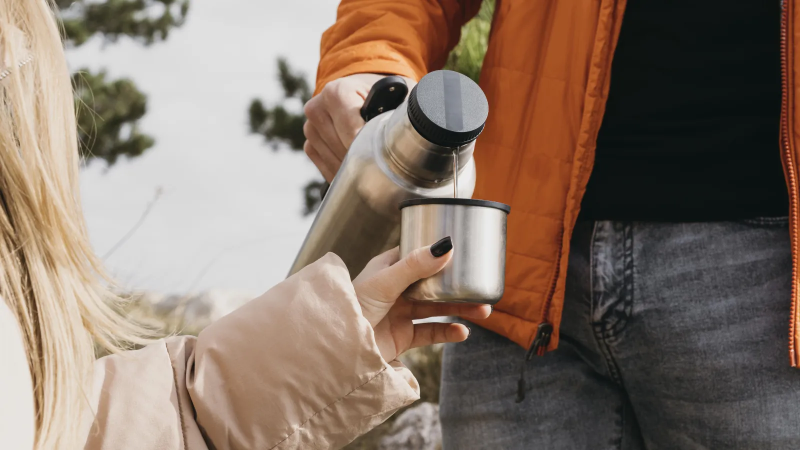 Pouring a drink from an insulated flask into a metal cup at camp