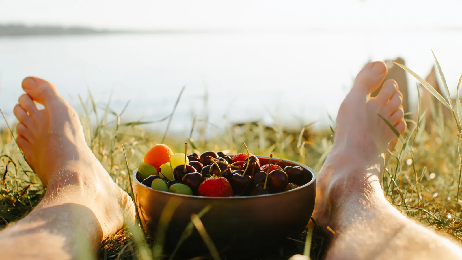 Bowl of cherries and strawberries in the grass beside a lake at camp