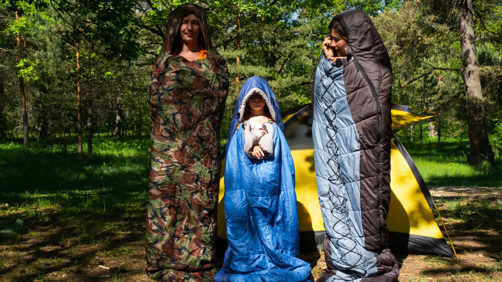 Three campers standing wrapped in their sleeping bags outside a tent