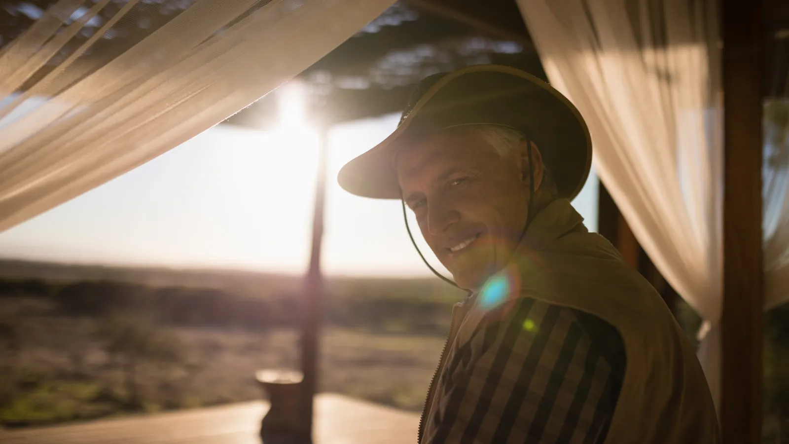 Camper in a wide-brim hat under a shelter with the low morning sun behind him