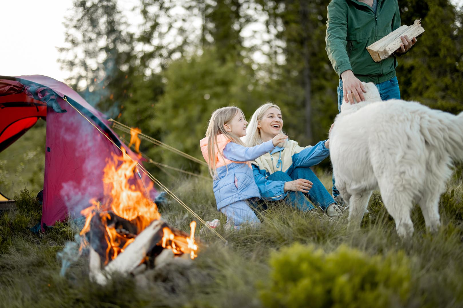 Young family sit by campfire near tent nature