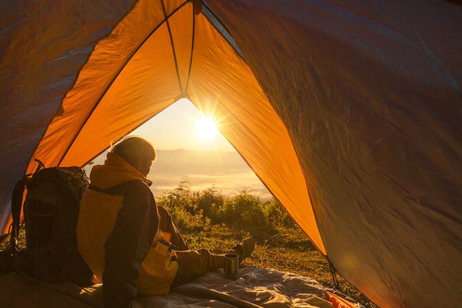 Young man sitting tent looking mountain landscape winter
